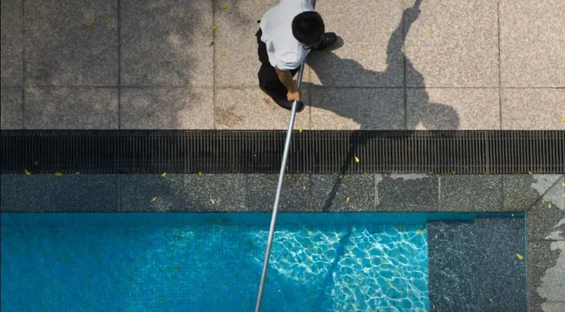 Vue du dessus d'un agent retirant les feuilles d'une piscine avec une épuisette