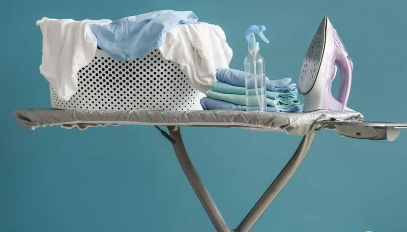 Table à repasser avec panier de linge, fer et vêtements pliés